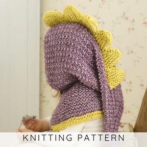 Puede incluir: Una capucha de dinosaurio tejida en morado y amarillo. La capucha está hecha de una tela de punto grueso con una apariencia texturizada. La capucha tiene una fila de púas amarillas en la parte superior y un ribete amarillo. El texto "KNITTING PATTERN" está en la parte inferior.