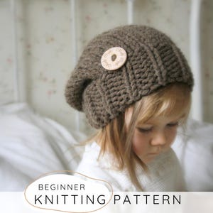 Puede incluir: Un gorro tejido marrón con un botón de madera. El gorro es de punto acanalado y tiene un ajuste holgado. El texto "BEGINNER KNITTING PATTERN" se muestra en un óvalo blanco en la parte inferior de la imagen.
