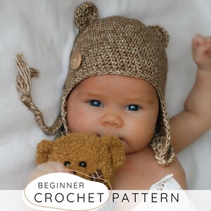 Puede incluir: Un gorro de ganchillo color canela con orejas de oso, que presenta un pequeño botón de madera en el lateral y lazos trenzados. El gorro tiene una textura de punto denso. El texto en la parte inferior dice: BEGINNER CROCHET PATTERN.