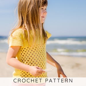 Puede incluir: Un top amarillo de ganchillo con un diseño calado. La imagen muestra el texto "CROCHET PATTERN" en la parte inferior. El top tiene mangas cortas y cuello redondo. El fondo es una playa con el océano y el cielo.