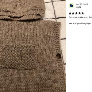 May include: A knitted, hooded vest in a neutral brown color. The vest features a front pocket and is fastened with two large, round buttons. The hood is attached to the vest. The text "Easy to make and beautiful" is visible.
