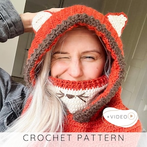 May include: A crocheted fox hood in shades of orange, brown, and white. The hood features fox ears and a face design on the front. The text "CROCHET PATTERN" is displayed at the bottom of the image.