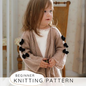 Puede incluir: Una niña lleva una rebeca de punto marrón claro con lazos negros en las mangas. La rebeca abierta está hecha de un hilo suave y de tejido abierto. El texto "BEGINNER KNITTING PATTERN" se muestra en la parte inferior.