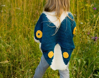 Puede incluir: Capa de ganchillo hecha a mano en azul marino, blanco y amarillo, con diseño de mariposa. La capa presenta detalles circulares amarillos y la lleva un niño. El texto "CROCHET PATTERN" está en la parte inferior de la imagen.