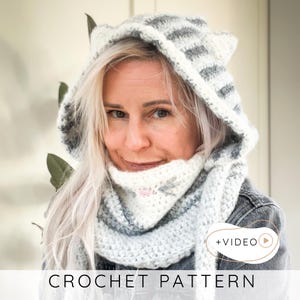 May include: A crocheted cat hood and scarf set in white and gray. The hood features cat ears and gray stripes. The scarf is white with gray accents and a small pink detail. The text "CROCHET PATTERN" is at the bottom of the image.