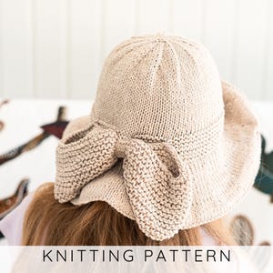 Puede incluir: Un sombrero de sol de punto beige con ala ancha y lazo decorativo. El sombrero está hecho de un hilo suave y texturizado y tiene un diseño clásico y femenino. El texto "KNITTING PATTERN" está en la parte inferior de la imagen.