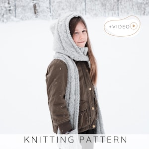 Könnte beinhalten: Eine Person trägt eine graue Strickhaube mit Ohrendetails und einen passenden Schal. Die Person trägt eine braune Jacke und steht in einer verschneiten Umgebung. Der Text "KNITTING PATTERN" befindet sich am unteren Rand des Bildes.