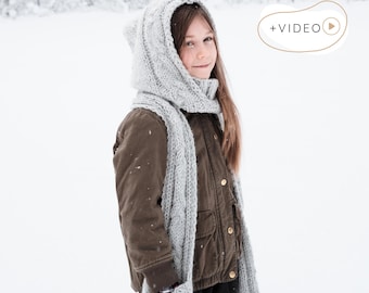 May include: A young person wearing a gray knitted hood with ear details and a matching scarf. The person is wearing a brown jacket and standing in a snowy environment. The text "KNITTING PATTERN" is at the bottom of the image.