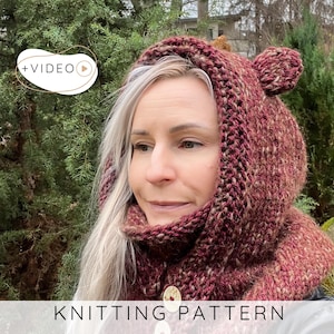 May include: A woman wearing a burgundy and tan knitted hood with bear ears. The hood is part of a knitted cowl, fastened with two decorative buttons. The text "KNITTING PATTERN" is displayed at the bottom of the image.