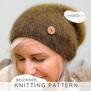 Può includere: Un berretto in maglia verde oliva soffice con un bottone rotondo in legno sul lato. Il berretto ha un aspetto morbido e testurizzato con un motivo a maglia visibile. Il testo "VIDEO" e "BEGINNER KNITTING PATTERN" è sovrapposto all'immagine.