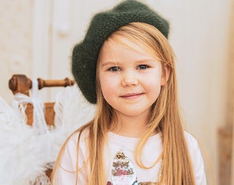 May include: A dark forest green fuzzy knit beret with a soft, textured surface. The hat features a classic rounded shape and is crafted from a fine, slightly brushed yarn. The text KNITTING PATTERN is displayed at the bottom of the image.