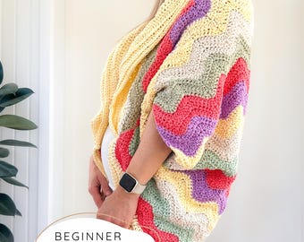 May include: A colorful, crochet cardigan in a chevron pattern. The cardigan features a mix of pastel colors including yellow, pink, purple, and green. The text "BEGINNER CROCHET PATTERN" is displayed at the bottom of the image.