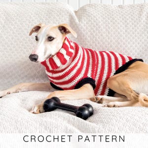 May include: A dog wearing a red and white striped crochet sweater with a black trim. The dog is lying on a white textured surface with a black bone-shaped toy. The text "CROCHET PATTERN" is at the bottom of the image.