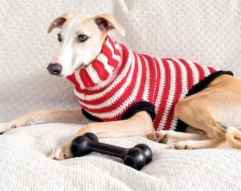 May include: A dog wearing a red and white striped crochet sweater with a black trim. The dog is lying on a white textured surface with a black bone-shaped toy. The text "CROCHET PATTERN" is at the bottom of the image.