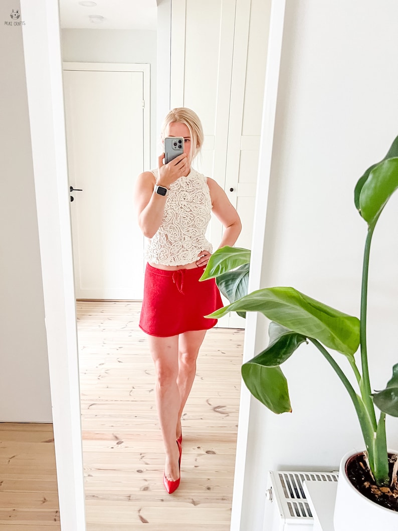 May include: A sleeveless, cream-colored lace top paired with a bright red mini skirt and matching red heels. The outfit is captured in a mirror, reflecting a modern, stylish ensemble. The image showcases a fashion-forward look.