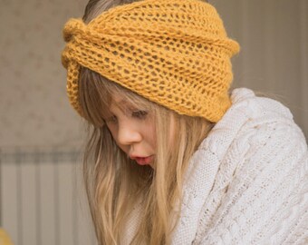May include: A mustard yellow knitted headband featuring an open, airy stitch pattern and a central twisted knot detail. The accessory is worn around the head, and the image includes the text KNITTING PATTERN at the bottom of the frame.