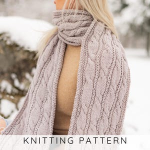 May include: A light mauve cable knit scarf featuring a repeating vertical braided pattern. The scarf is wrapped around the neck and draped over the shoulders. The text KNITTING PATTERN is printed in black at the bottom of the image.