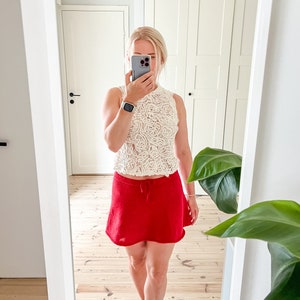 May include: A cream-colored, sleeveless lace top paired with a bright red mini skirt. The skirt has a drawstring waist. The outfit is completed with red heels. The image is taken in front of a mirror.