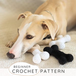 Könnte beinhalten: Ein hellbrauner Hund liegt neben drei gehäkelten Hundeknochen-Spielzeugen in Weiß, Schwarz und Hellbraun. Die Spielzeuge liegen auf einer cremefarbenen Oberfläche. Der Text unten lautet "BEGINNER CROCHET PATTERN".