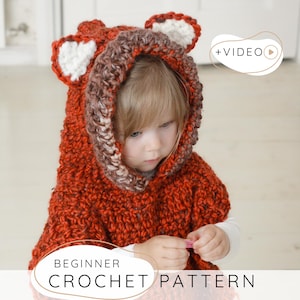 May include: A child wearing a handmade orange crochet fox hood with white and brown accents. The hood has fox ears and a textured appearance. The text "BEGINNER CROCHET PATTERN" is displayed at the bottom of the image.