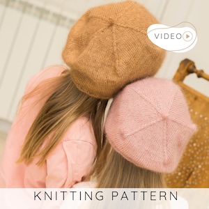 May include: Two knitted berets, one in a warm brown and the other in a soft pink, are shown. The berets are resting on a person's head. The text "KNITTING PATTERN" is displayed at the bottom of the image. A video icon is in the upper right corner.