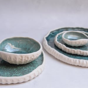 Peut inclure: Ensemble de quatre bols en céramique avec un bord blanc et un glaçage turquoise. Les bols sont imbriqués les uns dans les autres, le plus grand bol en bas et le plus petit bol en haut.