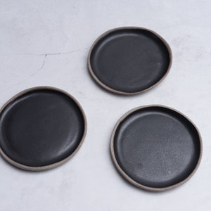 Puede incluir: Tres platos de cerámica negra con un borde ligeramente elevado. Los platos están sobre un fondo blanco.