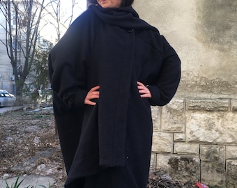 Può includere: Un cappotto nero a maniche lunghe con collo alto e design drappeggiato. Il cappotto è realizzato in un tessuto morbido e testurizzato e ha una vestibilità rilassata.