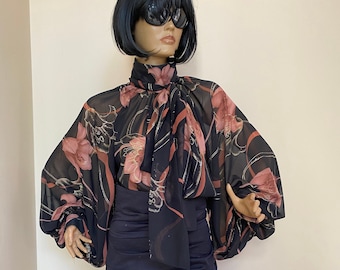 May include: A black and pink floral print blouse with a high neck and a bow tie. The blouse has long, puffy sleeves and is made of a sheer fabric.