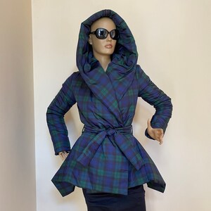 Può includere: Una giacca con cappuccio a quadri blu e verdi con un design avvolgente e una cintura. La giacca ha una silhouette aderente e un orlo leggermente svasato.