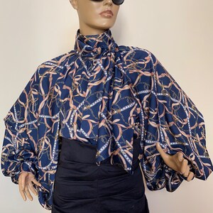 May include: A navy blue blouse with a pink and gold chain print. The blouse has a high neck and long sleeves with a gathered puff at the shoulder.