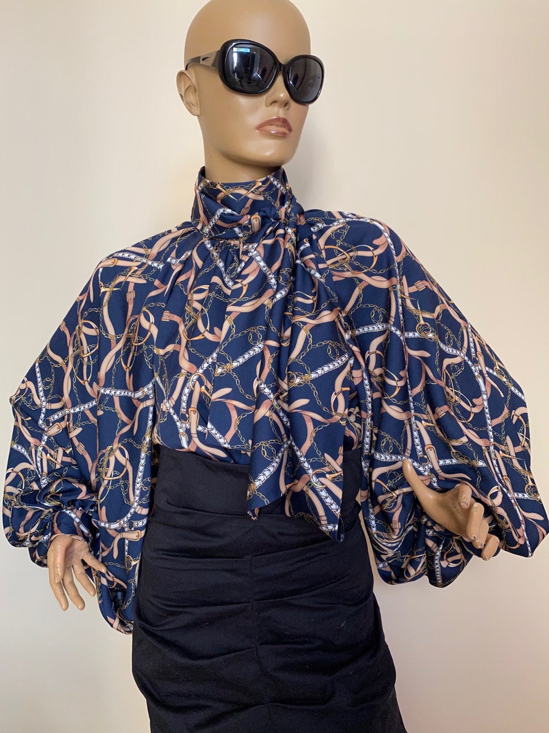 May include: A navy blue blouse with a pink and gold chain print. The blouse has a high neck and long sleeves with a gathered puff at the shoulder.