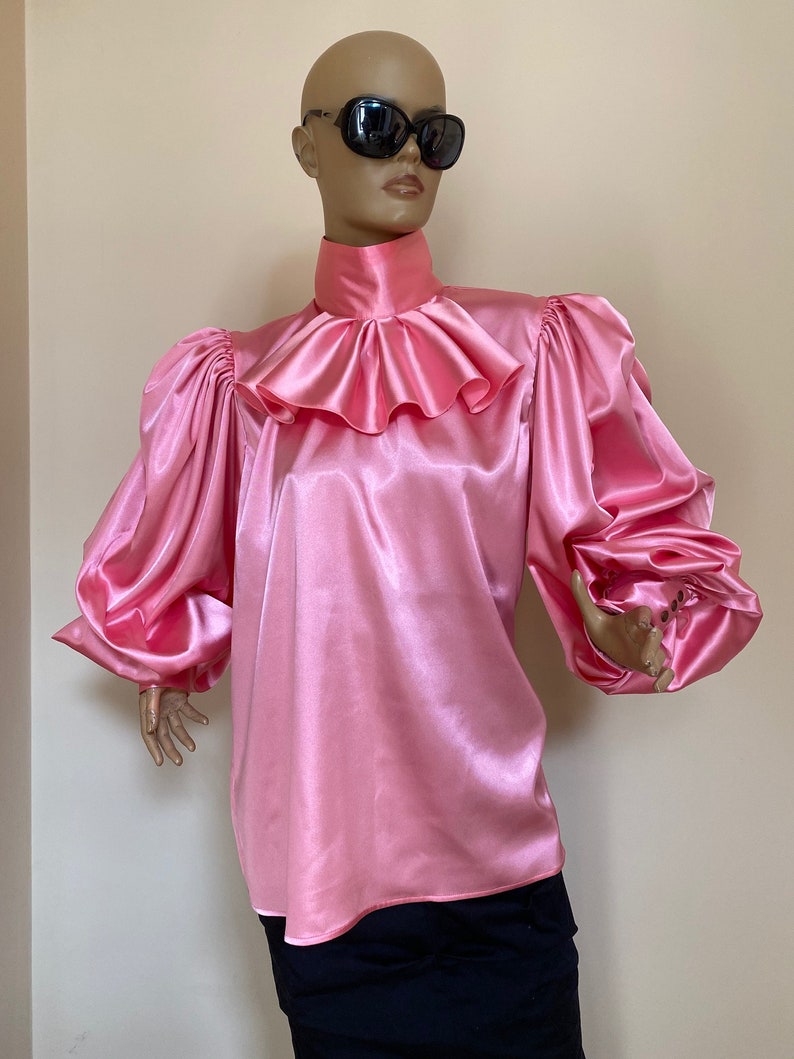 May include: A pink satin blouse with a high ruffled collar and long, puffed sleeves.