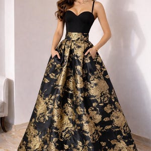 May include: A formal black gown with a sweetheart neckline and spaghetti straps. The full skirt features a gold floral brocade pattern. The dress has pockets and is suitable for special occasions.
