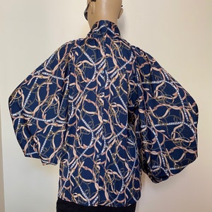 May include: A navy blue blouse with a chain and ribbon print. The blouse has long, puffed sleeves and a high neck.