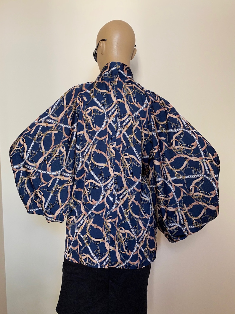 May include: A navy blue blouse with a chain and ribbon print. The blouse has long, puffed sleeves and a high neck.