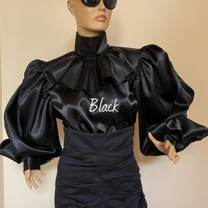 May include: A black satin blouse with a high ruffled collar and large, puffed sleeves. The blouse has the word "Black" embroidered on the front.