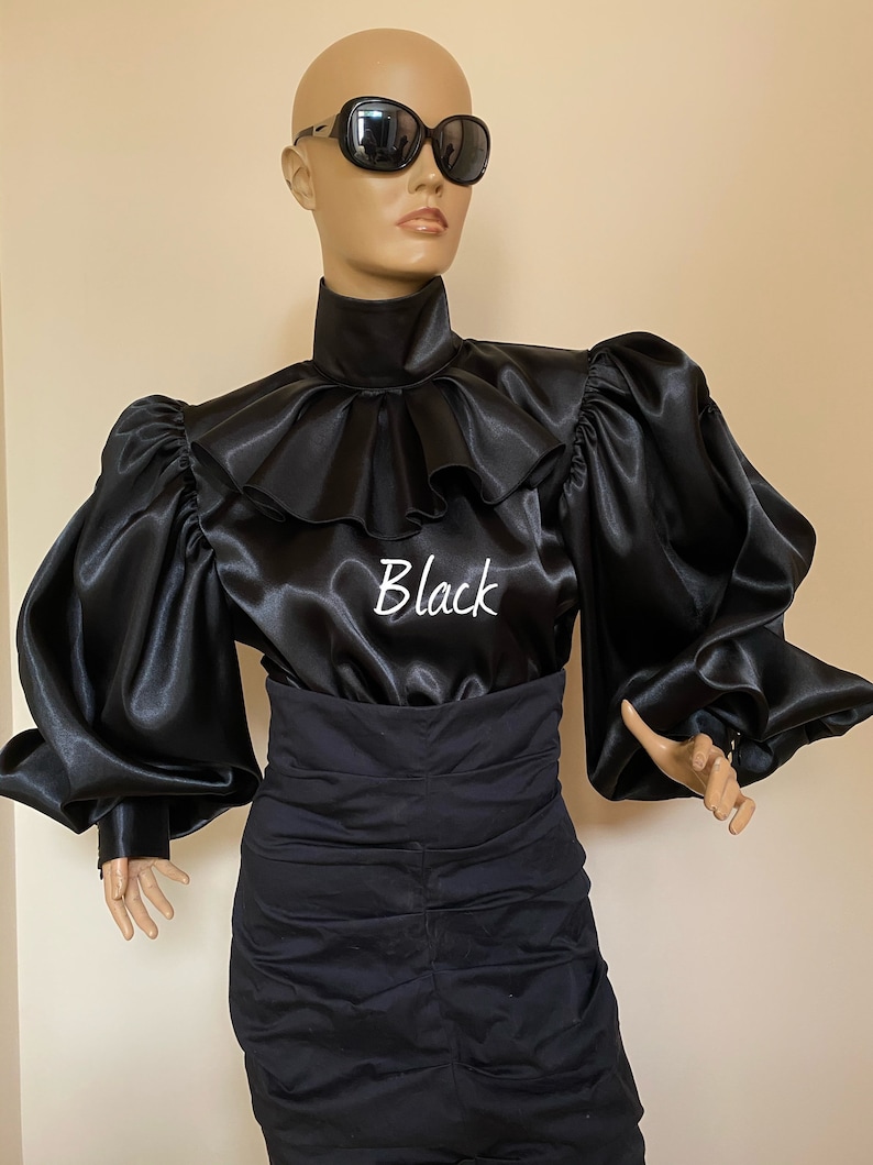 May include: A black satin blouse with a high ruffled collar and large, puffed sleeves. The blouse has the word "Black" embroidered on the front.