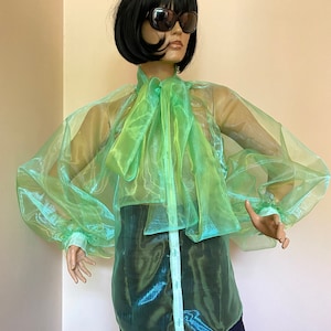 May include: A sheer green blouse with a large bow at the neck. The blouse has long, puffed sleeves and a button-up front.