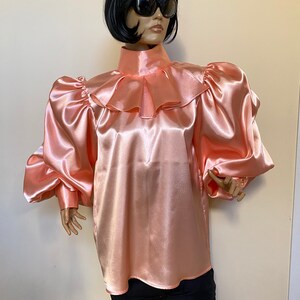 May include: A peach-colored satin blouse with a high ruffled collar and long, puffed sleeves.