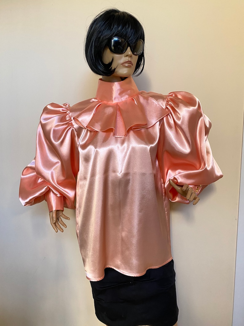 May include: A peach-colored satin blouse with a high ruffled collar and long, puffed sleeves.