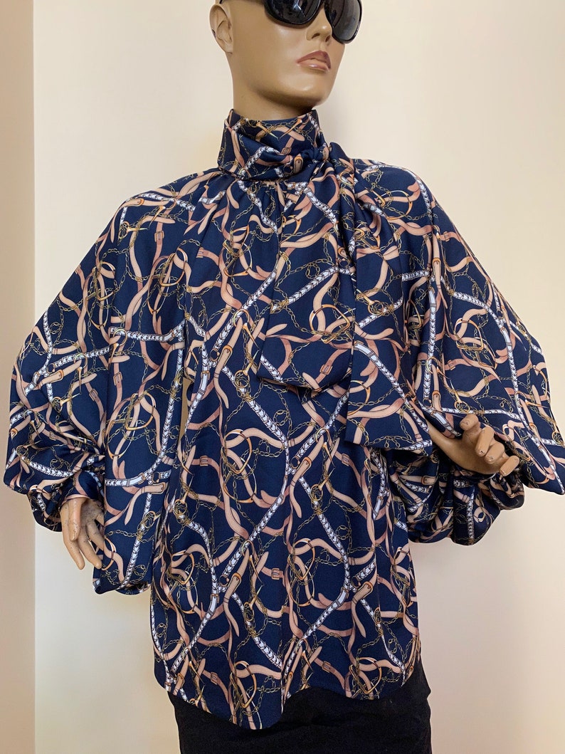 May include: A navy blue blouse with a high neck and long sleeves. The blouse has a pattern of gold chains and brown belts.