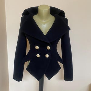 May include: A navy blue double-breasted jacket with a unique design. The jacket features a wide collar, four gold-colored buttons, and distinctive angular cutouts at the waist. The jacket is displayed on a mannequin.