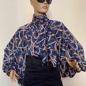 May include: A navy blue blouse with a chain and ribbon print. The blouse has a high neck and long sleeves with a gathered detail at the cuffs.