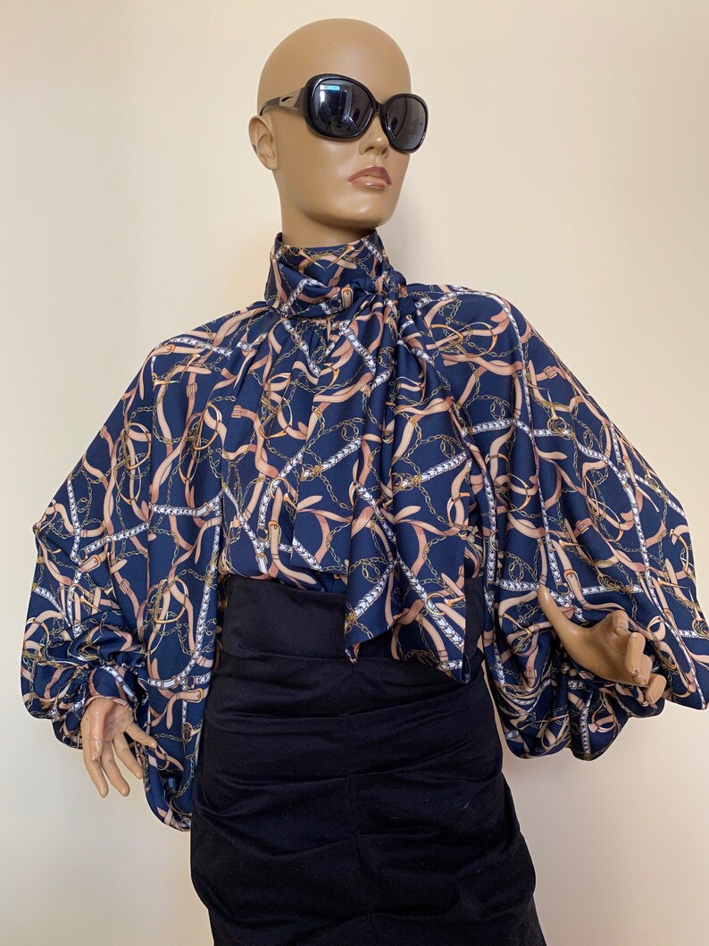 May include: A navy blue blouse with a chain and ribbon print. The blouse has a high neck and long sleeves with a gathered detail at the cuffs.