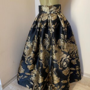 May include: A black and gold floral print skirt. The skirt is made of a shiny fabric and features a high waist and a full, flowing silhouette. The gold floral pattern is detailed and covers the entire skirt.