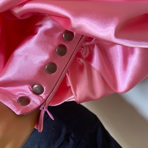May include: A pink satin blouse with a zipper and button closure on the sleeve. The buttons are silver and the zipper is black.