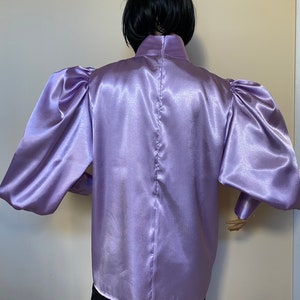 May include: A lilac satin blouse with long, puffed sleeves and a high, mock neck collar.
