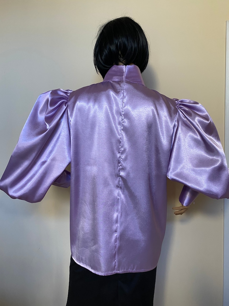May include: A lilac satin blouse with long, puffed sleeves and a high, mock neck collar.