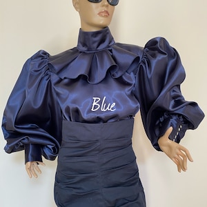May include: A navy blue satin blouse with a high ruffled collar and large, puffed sleeves. The blouse has the word "Blue" embroidered on the front.